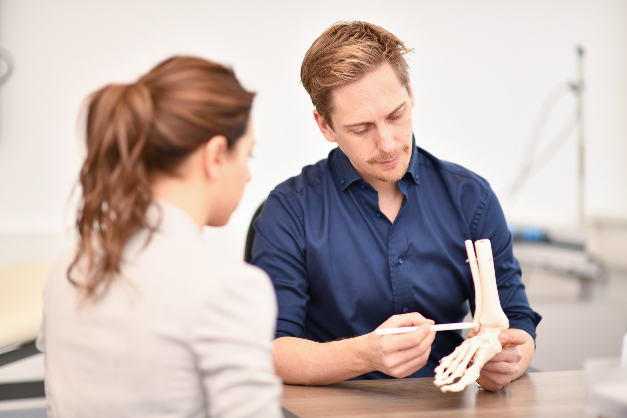 Mit einem Stift erklärt D. Treichler einer Patientin ihre Beschwerdebild an einem Modell eines Sprunggelenks