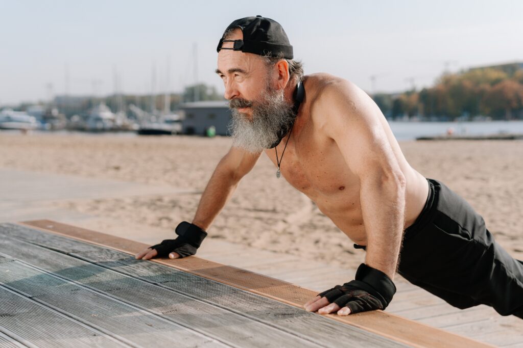 Ein Mann in Liegestützposition am Gehwegrand eines Strandes zeigt, dass Training im Alter möglich ist und tolle Ergebnisse bringt.