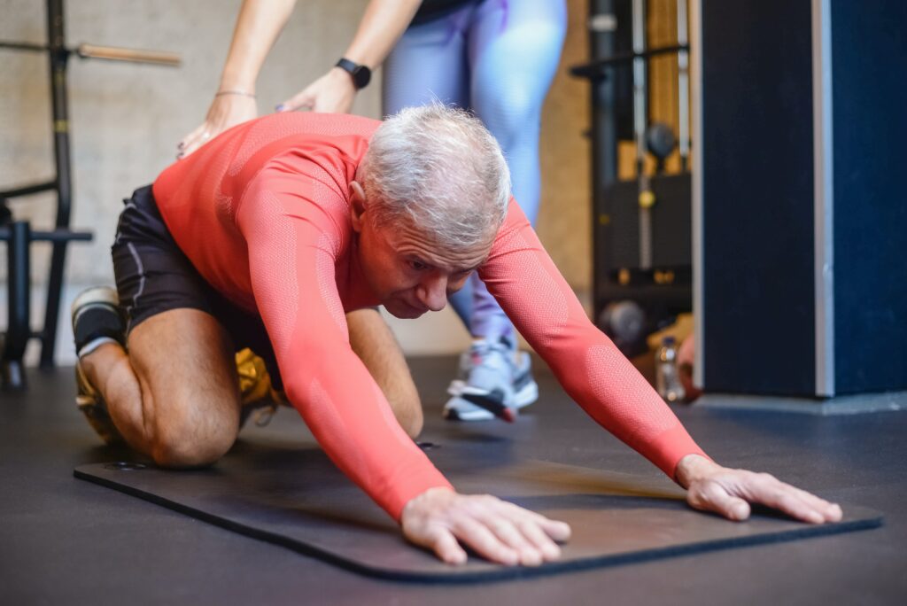 Ein Mann mit Osteoporose führt eine Rückendehnung aus unter Anleitung einer Therapeutin.